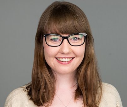 Smiling woman with black glasses and brown, shoulder length hair, wearing a cream sweater.