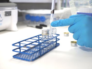 Hand in blue latex glove pipetting into clear tubes in a blue tube rack